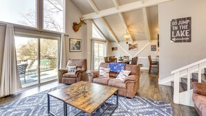 A spacious living room with a large window, a wooden coffee table, and a leather sofa. - Dock, Boat Slip & View: Lakefront Tan-Tar-A Home! (Osage Beach)