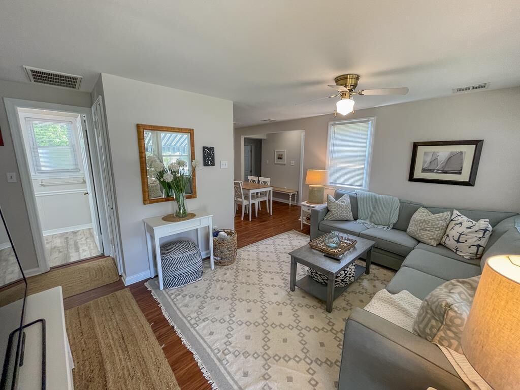 A living room with a gray sofa, a coffee table, and a lamp. There is a dining area with a table and chairs in the background.
