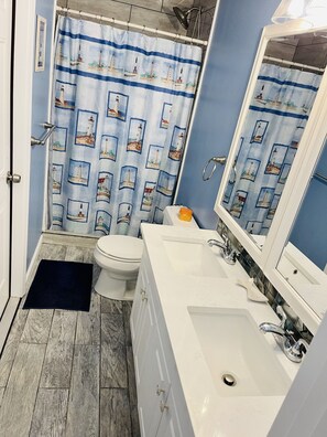 A bathroom with a white sink, a mirror, a toilet, and a shower curtain with a lighthouse pattern. - *Blue- tiful Views*  (Surfside Beach)