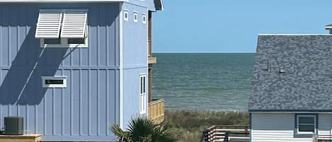 A coastal house with a balcony overlooking the sea, a wooden deck, and a fenced yard.