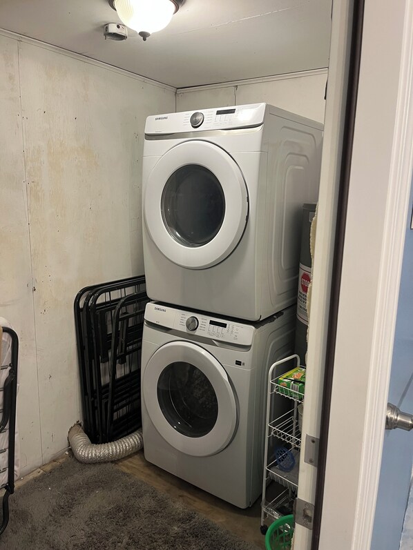 A laundry room with two stacked washing machines, a metal rack, and a storage cart. - *Blue- tiful Views* (Surfside Beach)