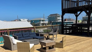 A wooden deck with outdoor furniture, including sofas and chairs, overlooking a beach area with houses in the background. - *Blue- tiful Views*  (Surfside Beach)