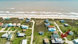 An aerial view of a coastal residential area with houses arranged in a grid pattern, a beach in the background, and a road running perpendicular to the houses. - *Blue- tiful Views*  (Surfside Beach)