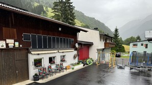 A building with a covered outdoor seating area, a red garage door, and a trampoline. - Sesselebenerhof by Interhome (See)
