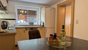 A compact kitchen with a window, a microwave, a refrigerator, and a dining area with a table. - Sesselebenerhof by Interhome (See)