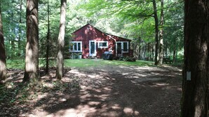 A rustic cabin with a porch, surrounded by dense forest. - Waterfront Cottage on Scenic Sportsman Pond (Fitzwilliam)