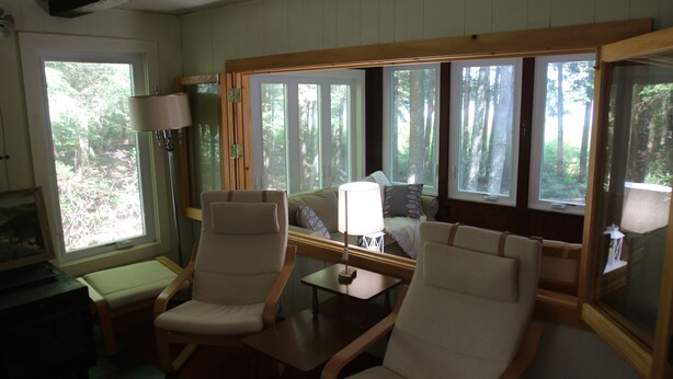 A cozy room with a large window, a sofa, two armchairs, a small table, and a lamp. - Waterfront Cottage on Scenic Sportsman Pond (Fitzwilliam)