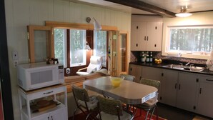 A compact kitchen with a dining area, a microwave, and a chair near the window. - Waterfront Cottage on Scenic Sportsman Pond (Fitzwilliam)