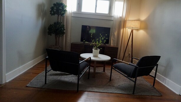 Una sala de estar con televisor, dos sillones, una mesita, una lámpara de pie y una planta en maceta.