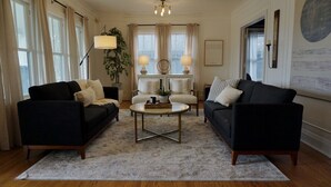 A living room with two black sofas, a round coffee table, and a large window with curtains.
