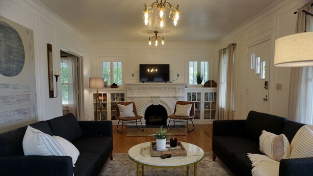 A living room with two black sofas, a white coffee table, a fireplace, and a television on the wall.