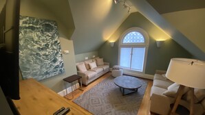 Una sala de estar estilo loft acogedora, con techo alto, un ventanal grande, una mesa de centro redonda y un sofá.