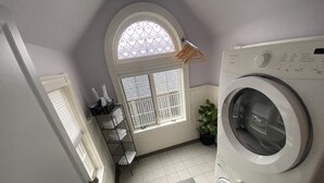 Un lavadero con lavadora, un tendedero, una ventana con persianas y una planta en maceta.