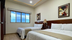 Quarto de hotel com duas camas de solteiro, uma cama grande, uma janela com vista e um quadro na parede.