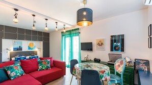 A modern living room with a red sofa, a dining table with floral tablecloth, and a kitchen area with green cabinets. - Sleeps 8, Pet Friendly, Garden & Roof Terrace (Split)