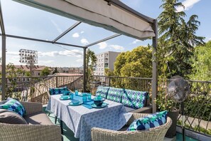 An outdoor patio with wicker furniture, a table set with blue and white tablecloths, and a fan. - Sleeps 8, Pet Friendly, Garden & Roof Terrace (Split)