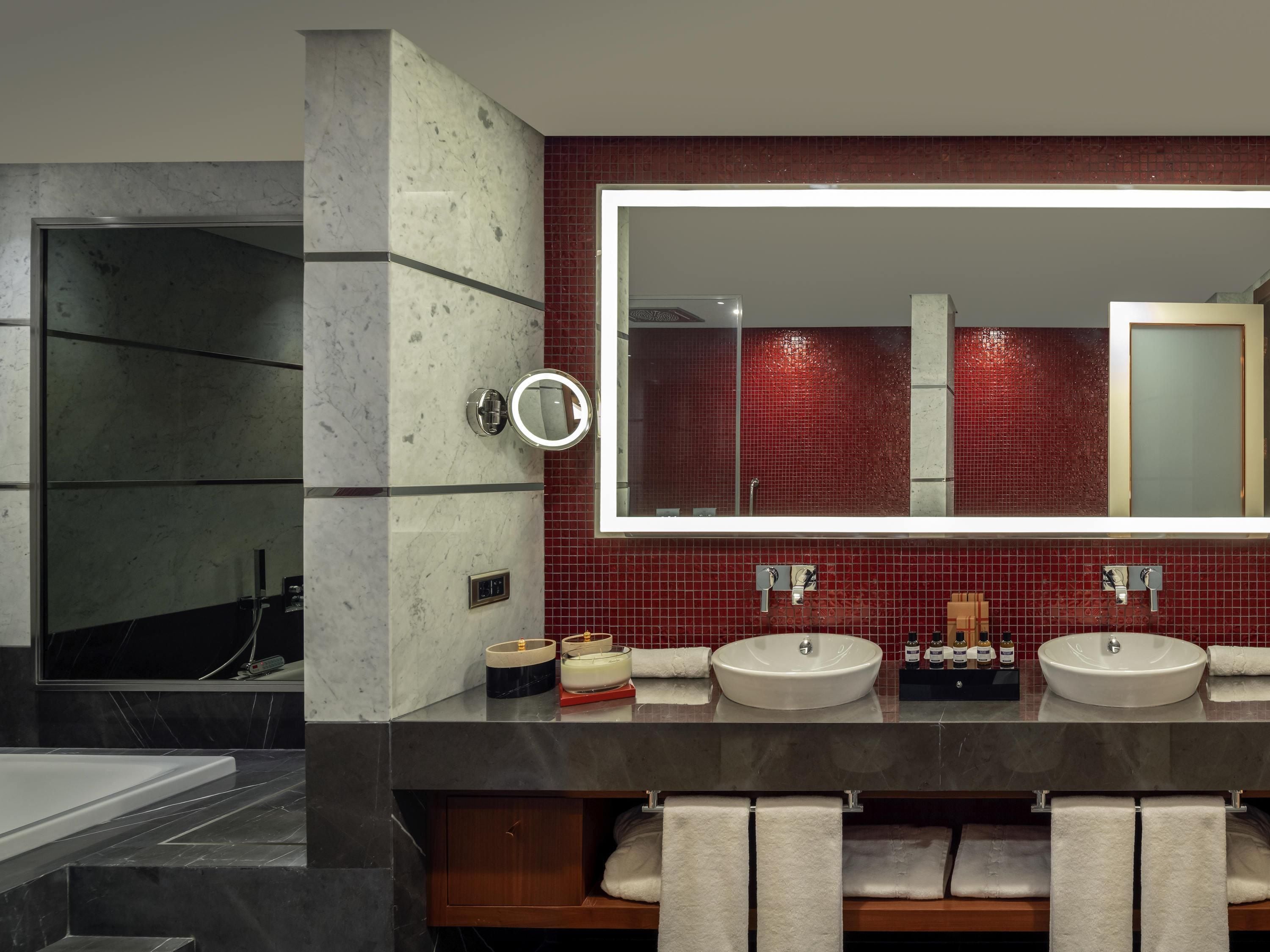A modern bathroom with two sinks, a large mirror, and a red-tiled wall.