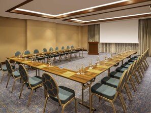 Un salón de conferencias con una larga mesa, sillas, un atril y una pantalla.
