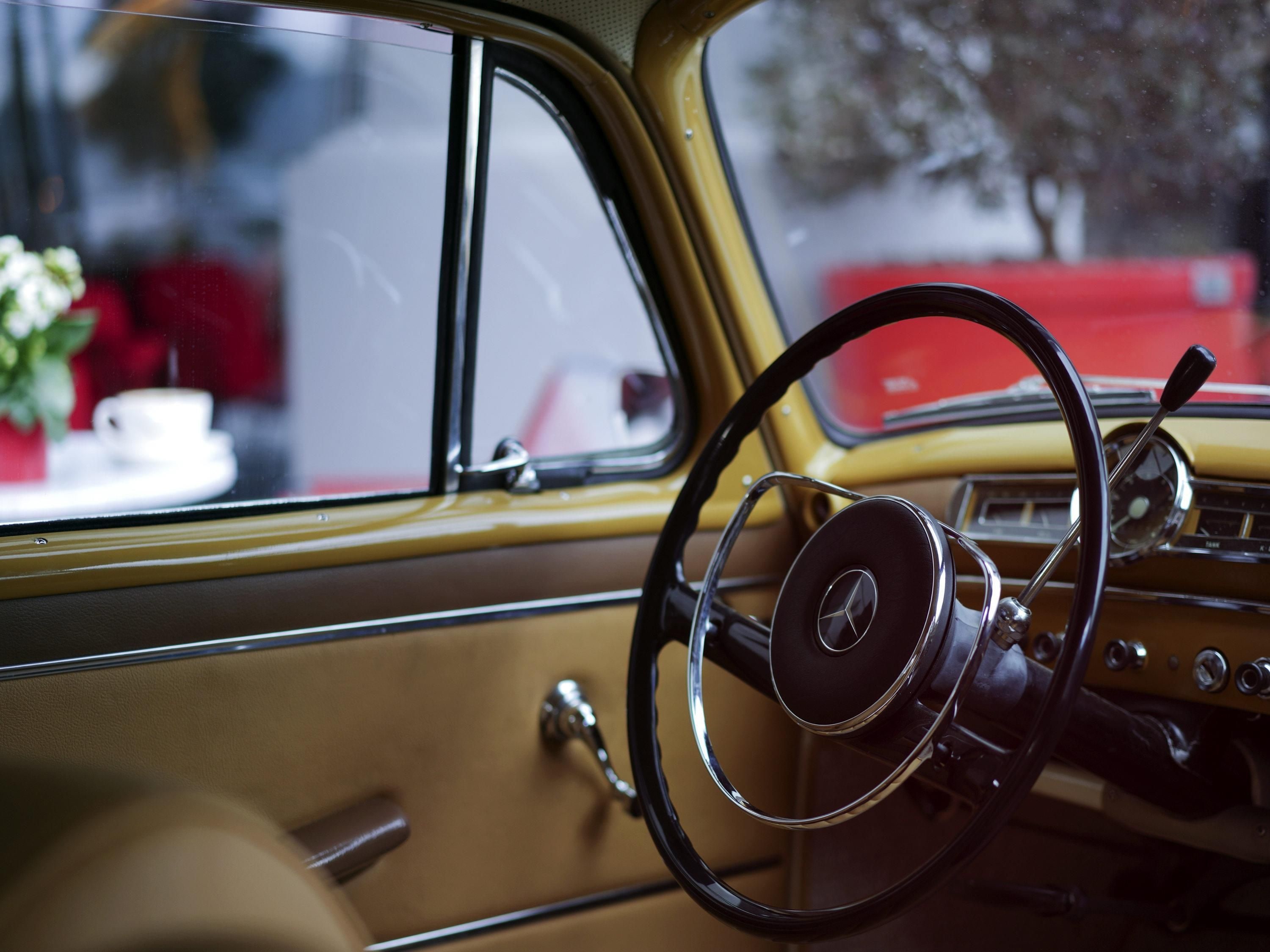 A vintage car interior with a steering wheel, dashboard, and door panel.