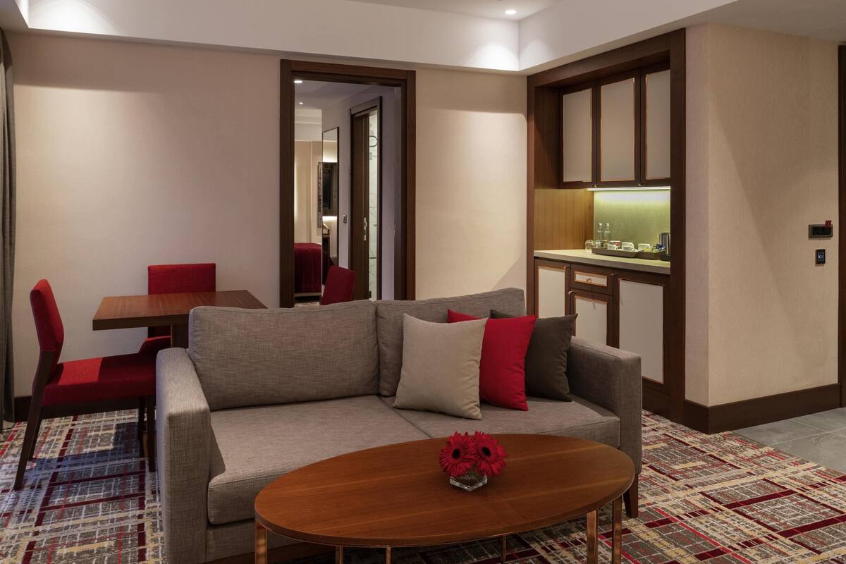 Quarto de hotel moderno com sofá, mesa de jantar e cozinha compacta.