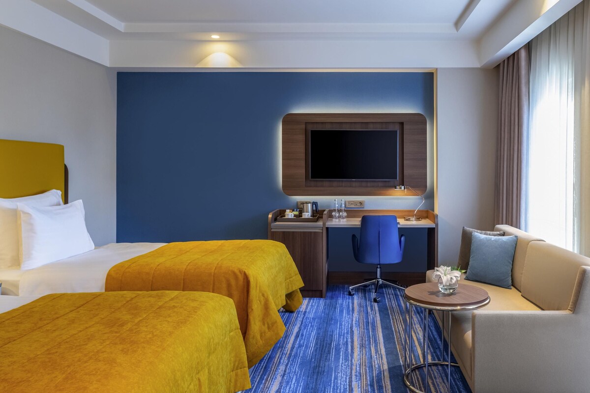 A hotel room with two beds, a desk, a chair, and a sofa.