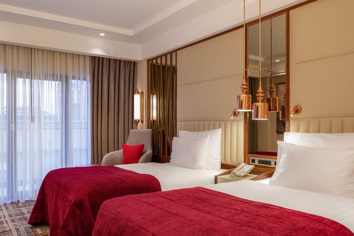 A hotel room with two beds, a large mirror, a chair, and a telephone on the nightstand.