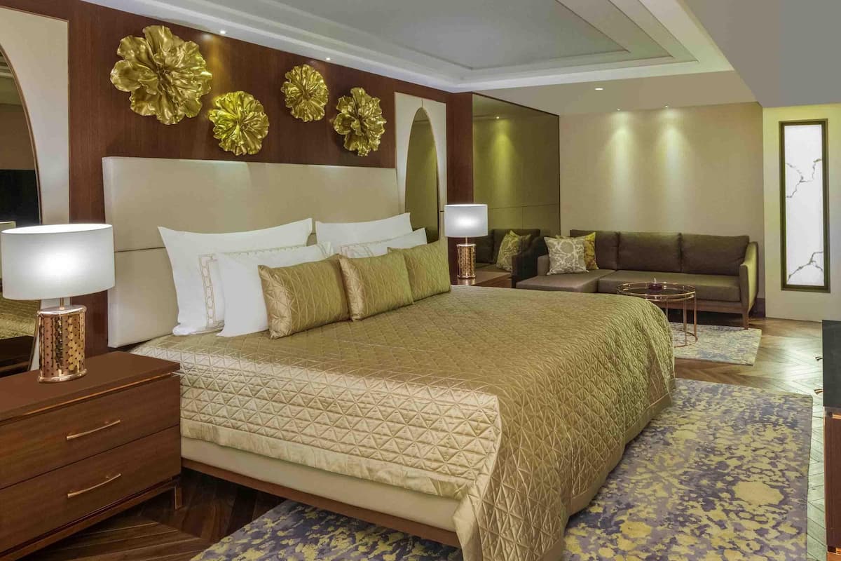 A spacious bedroom with a large bed, a sitting area with a sofa, and decorative wall art.