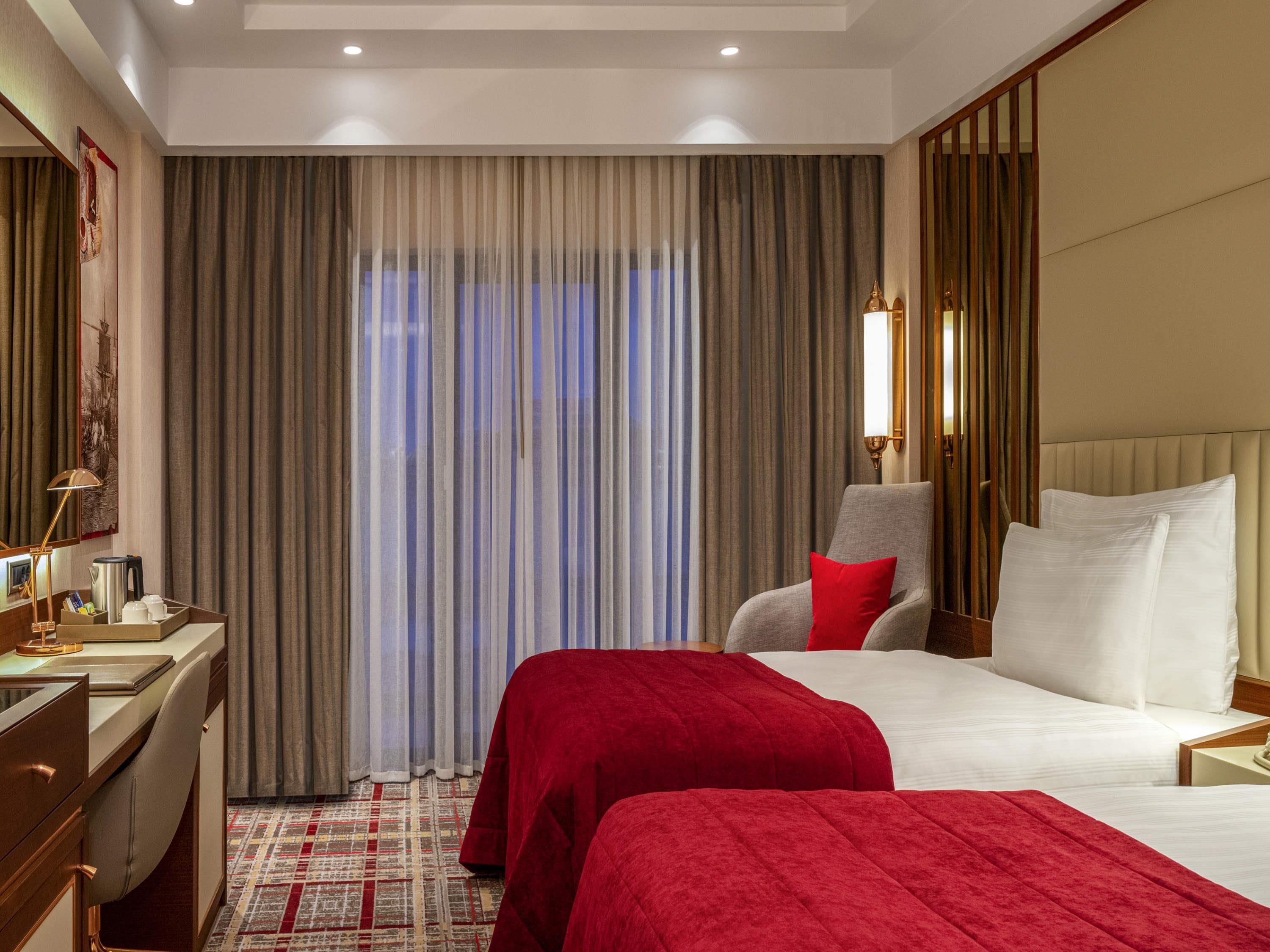 A hotel room with a bed, a desk, a chair, and a large window with curtains.