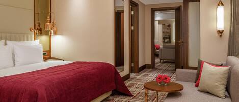 A hotel room with a large bed, a sofa, a small table with a vase of flowers, and a mirror.
