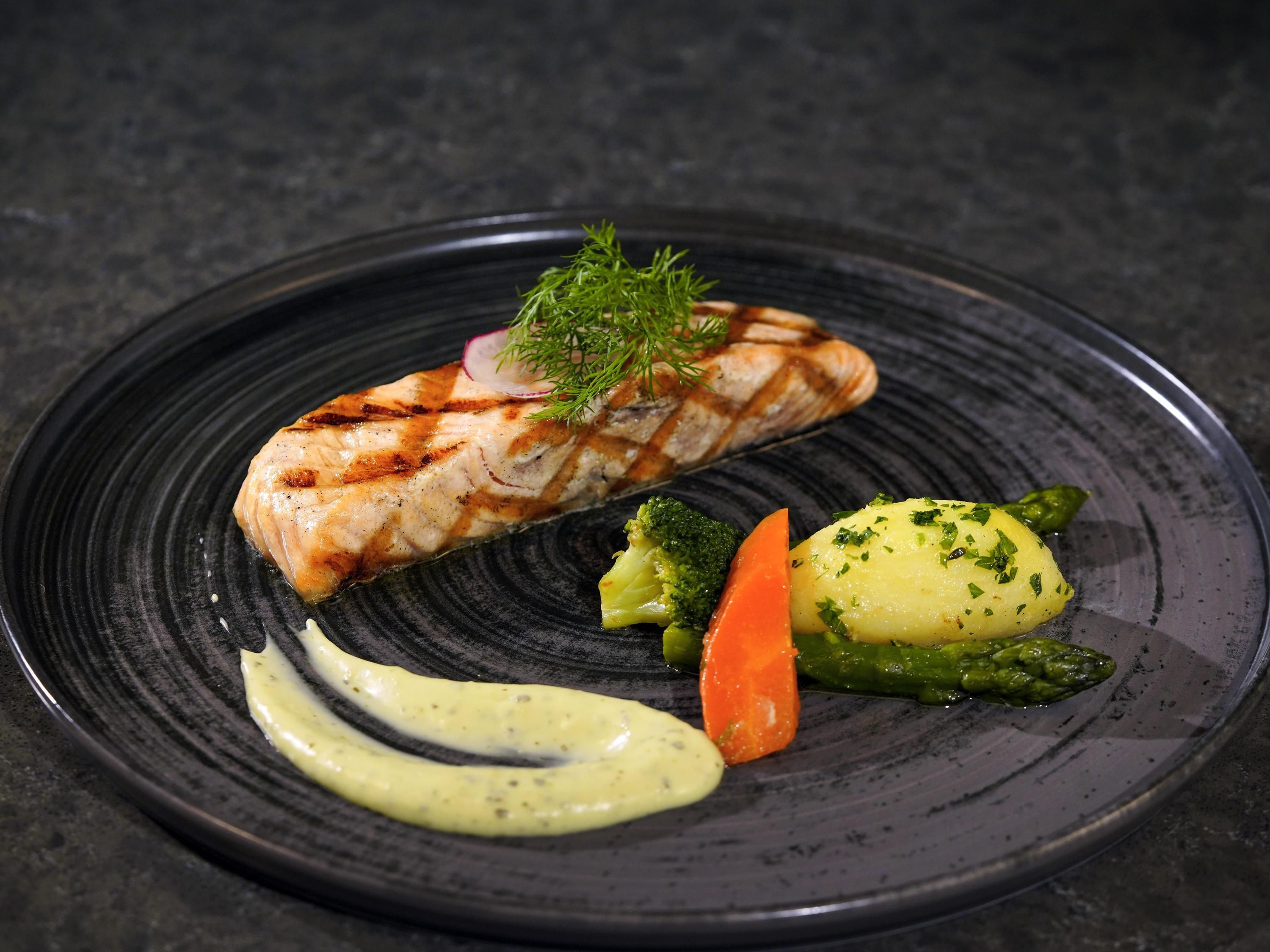 A plate with grilled salmon, broccoli, carrot, and mashed potatoes, garnished with herbs.