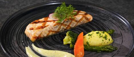 A plate with grilled salmon, broccoli, carrot, and mashed potatoes, garnished with herbs.