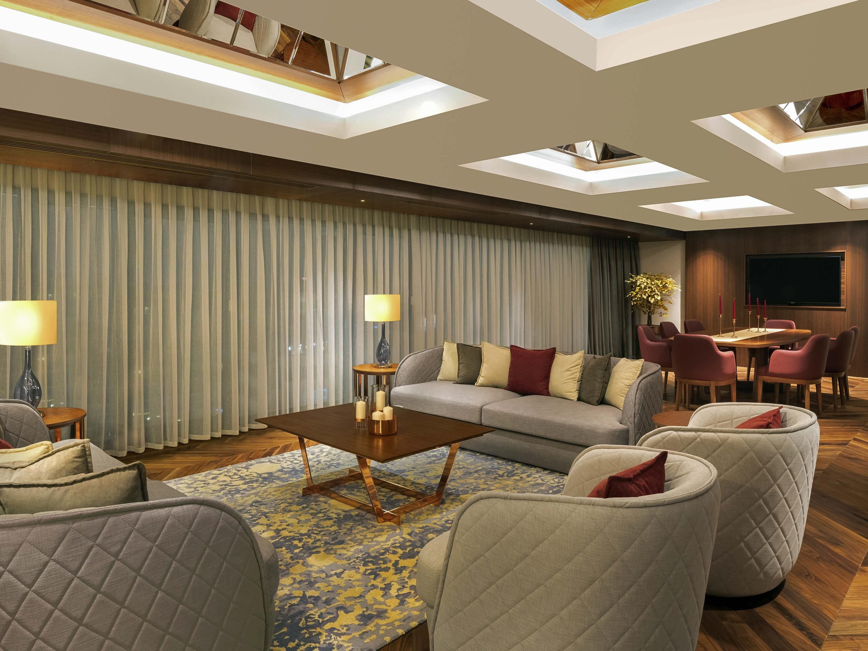 A modern living room with a sofa, armchairs, a coffee table, and a dining area with a table and chairs.