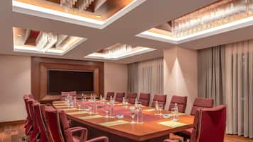 Un salón de conferencias con una larga mesa, sillas rojas y una pantalla grande.