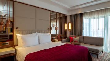 Ein Hotelzimmer mit einem großen Bett, einem Schlafsofa, einem Nachttisch, einem Spiegel und einem Fenster mit Vorhängen.