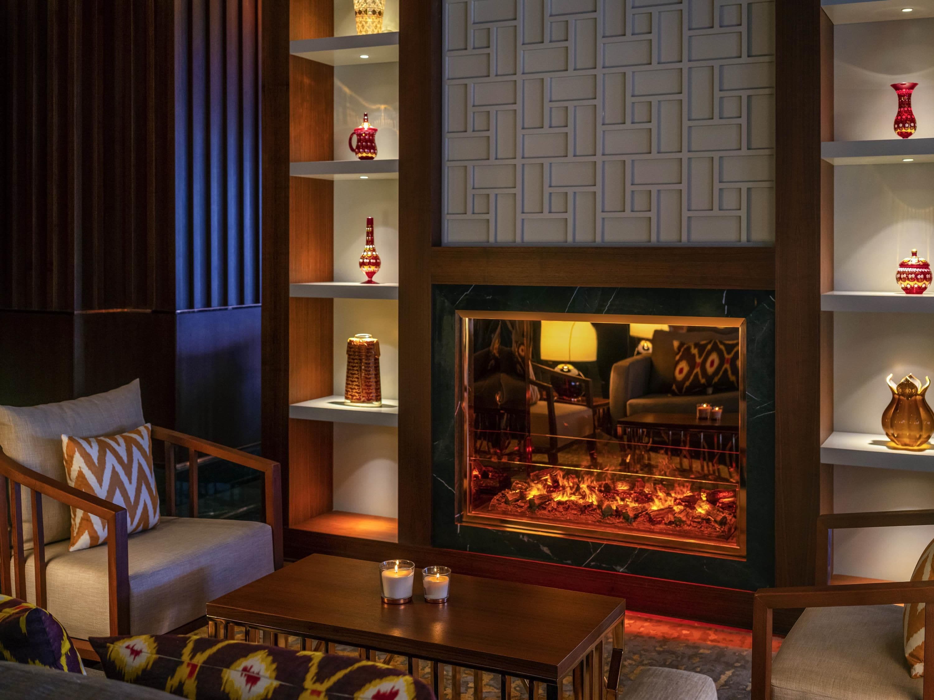 A cozy lounge area with a fireplace, seating, and decorative shelves.