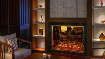 A cozy lounge area with a fireplace, seating, and decorative shelves.