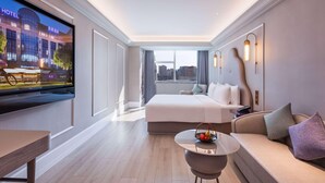 A modern hotel room with a large bed, a small round table with a fruit basket, a sofa, and a TV displaying a hotel sign. - Mercure Shijiazhuang People Square (Shijiazhuang)
