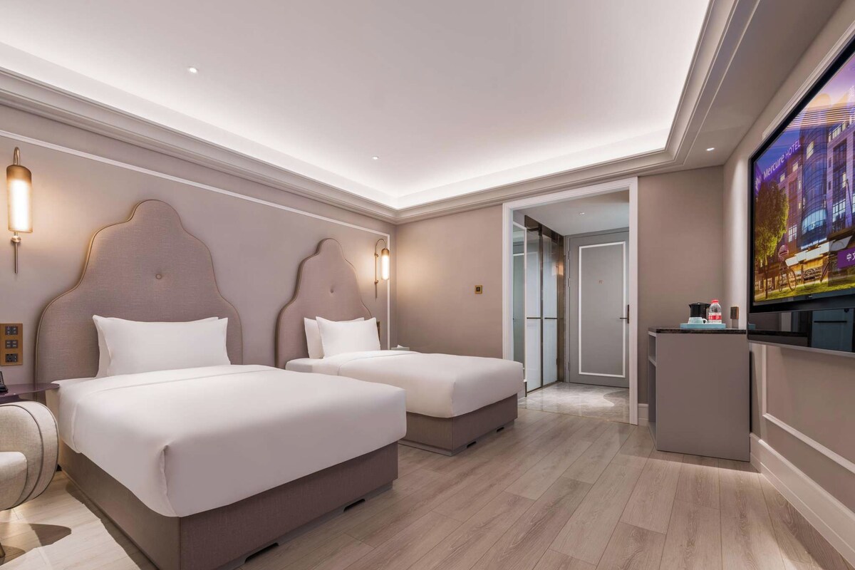A hotel room with two beds, a desk, a TV, and a door leading to a bathroom.