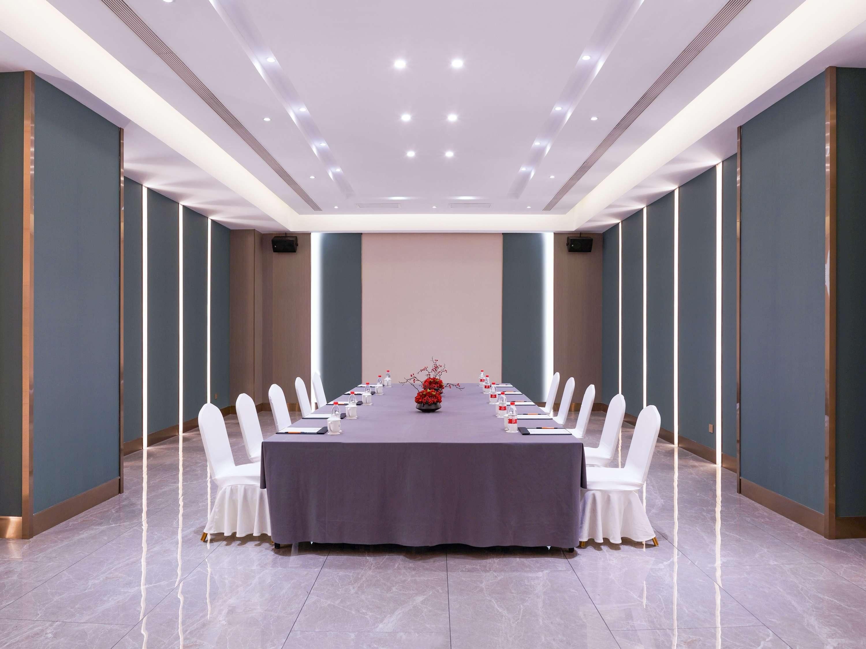A conference room with a long table, white chairs, and a grey tablecloth.