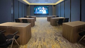 A conference room with a large screen at the front, multiple tables with chairs, and a patterned carpet. - Mercure Shijiazhuang People Square (Shijiazhuang)