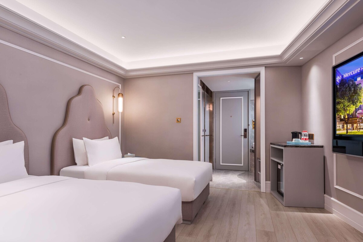 A hotel room with two beds, a TV, and a desk.