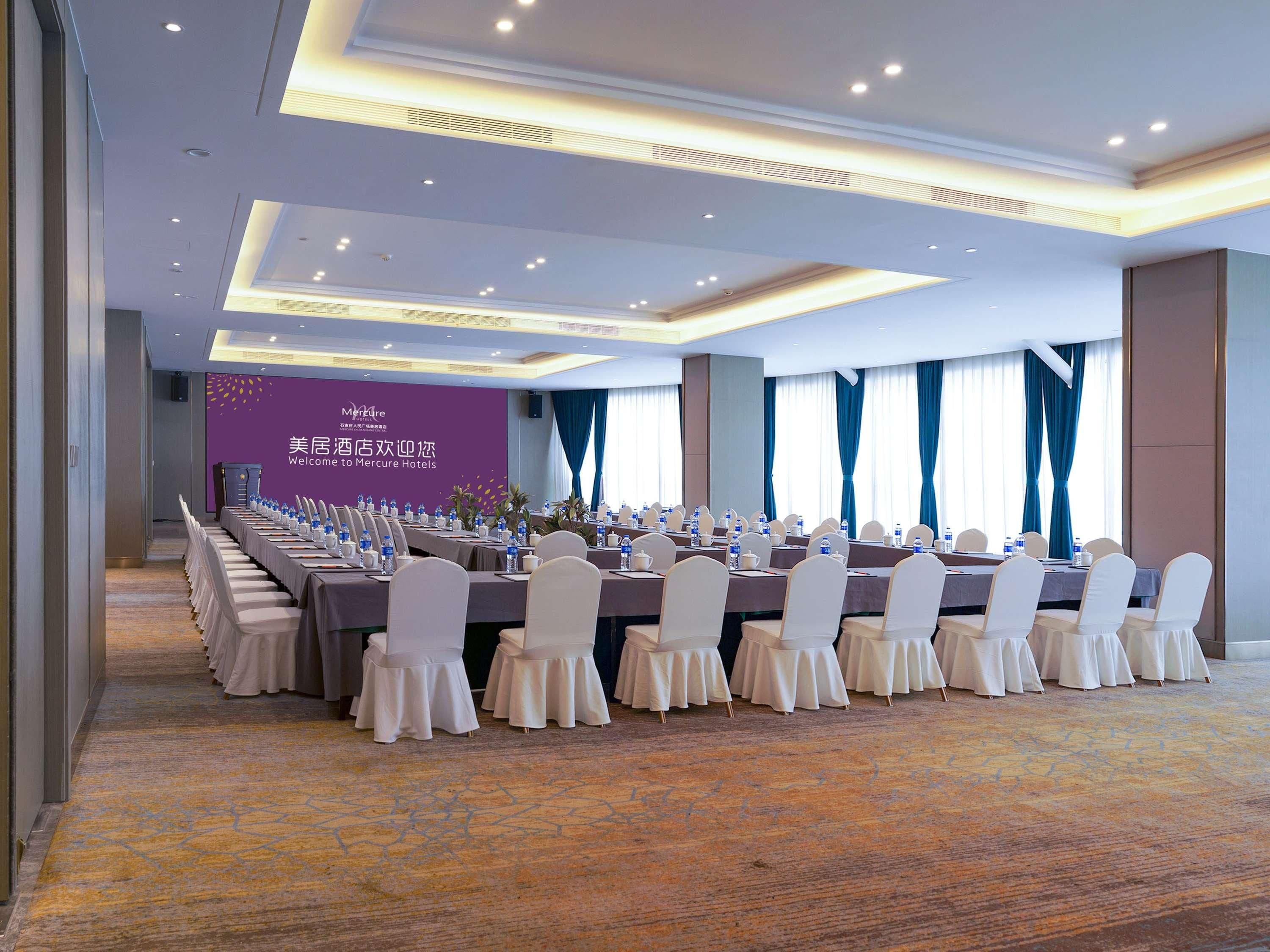 A conference room with a long table set for meetings, featuring a purple wall with a welcome sign, and a carpeted floor.