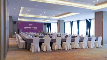 A conference room with a long table set for meetings, featuring a purple wall with a welcome sign, and a carpeted floor.