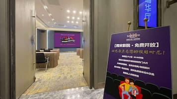 A hotel corridor with a conference room, a purple signboard with text, and a blue screen displaying a cartoon.