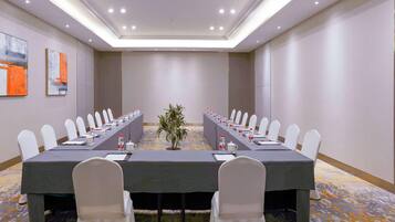 A conference room with a long table, white chairs, and a plant in the center.