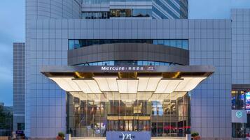 Une entrée d’hôtel moderne avec une façade en verre, une enseigne « Mercure » bien visible et une vue dégagée sur l’environnement urbain.