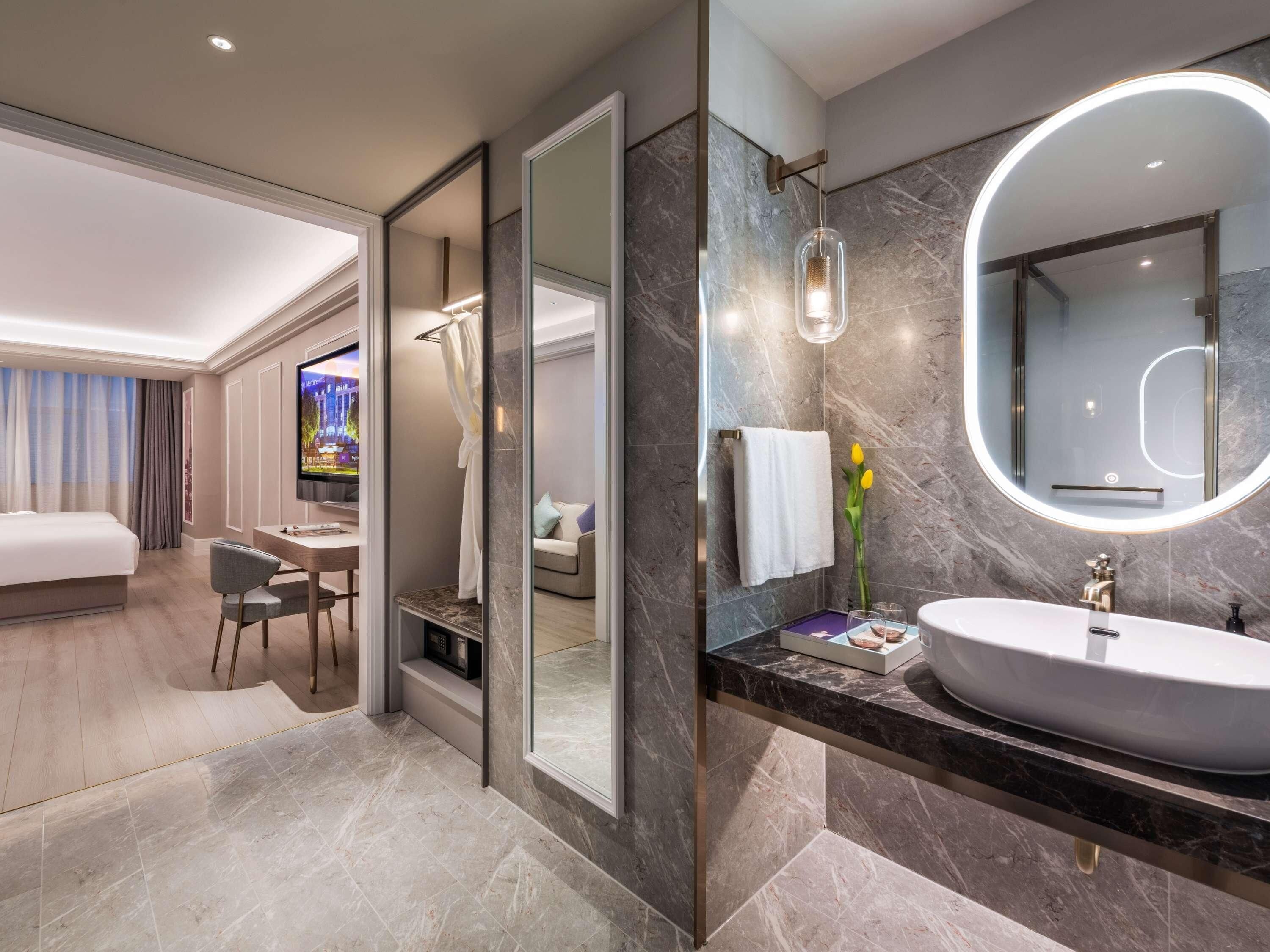 Une chambre d’hôtel moderne dotée d’un grand lit, d’un bureau avec une chaise, d’une télévision, d’une salle de bain avec un grand miroir et d’un lavabo.
