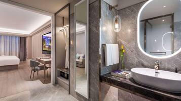Une chambre d’hôtel moderne dotée d’un grand lit, d’un bureau avec une chaise, d’une télévision, d’une salle de bain avec un grand miroir et d’un lavabo.