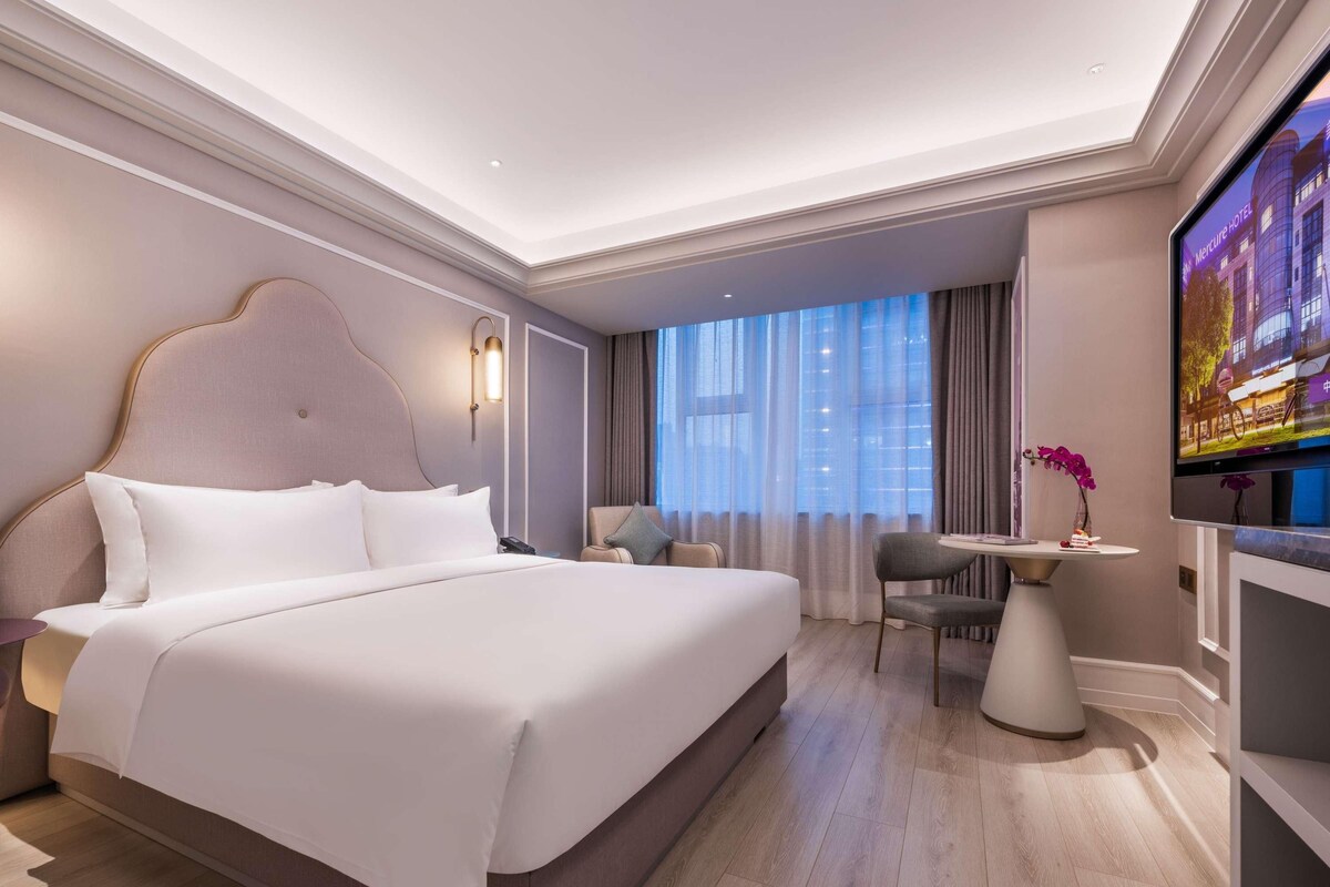 A modern hotel room with a large bed, a desk, and a TV.
