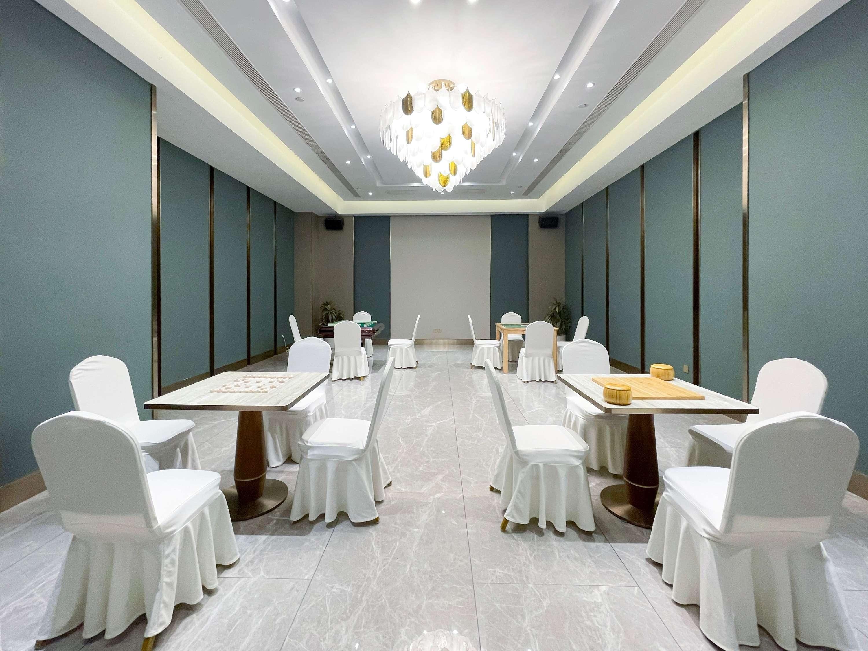 A conference room with a chandelier, white chairs, and tables set up for meetings.